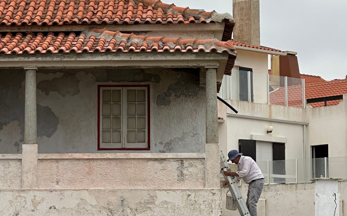 Profissional em escada realizando revestimento de fachada em reforma residencial